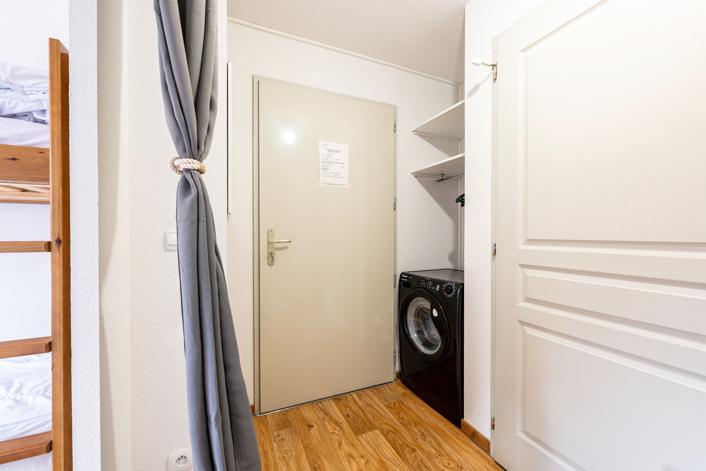 Un cuarto de lavado con lavadora, una puerta con un aviso y piso de madera.
