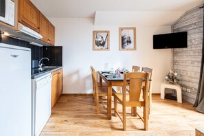 Ett kompakt kök med träskåp, diskmaskin och en matplats med bord och stolar.