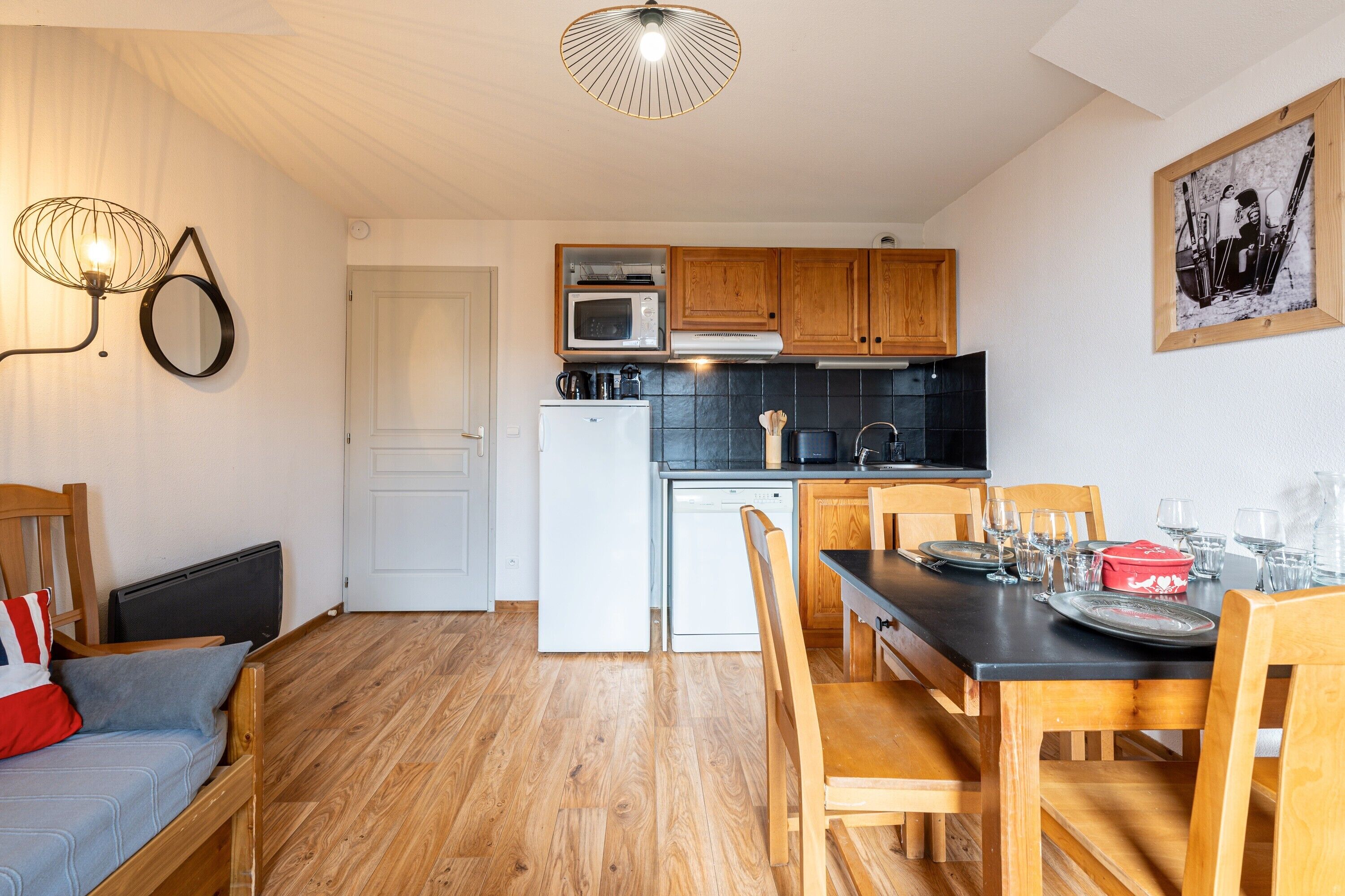 A compact kitchen with wooden cabinets, a microwave, a refrigerator, and a dining area with a table and chairs.