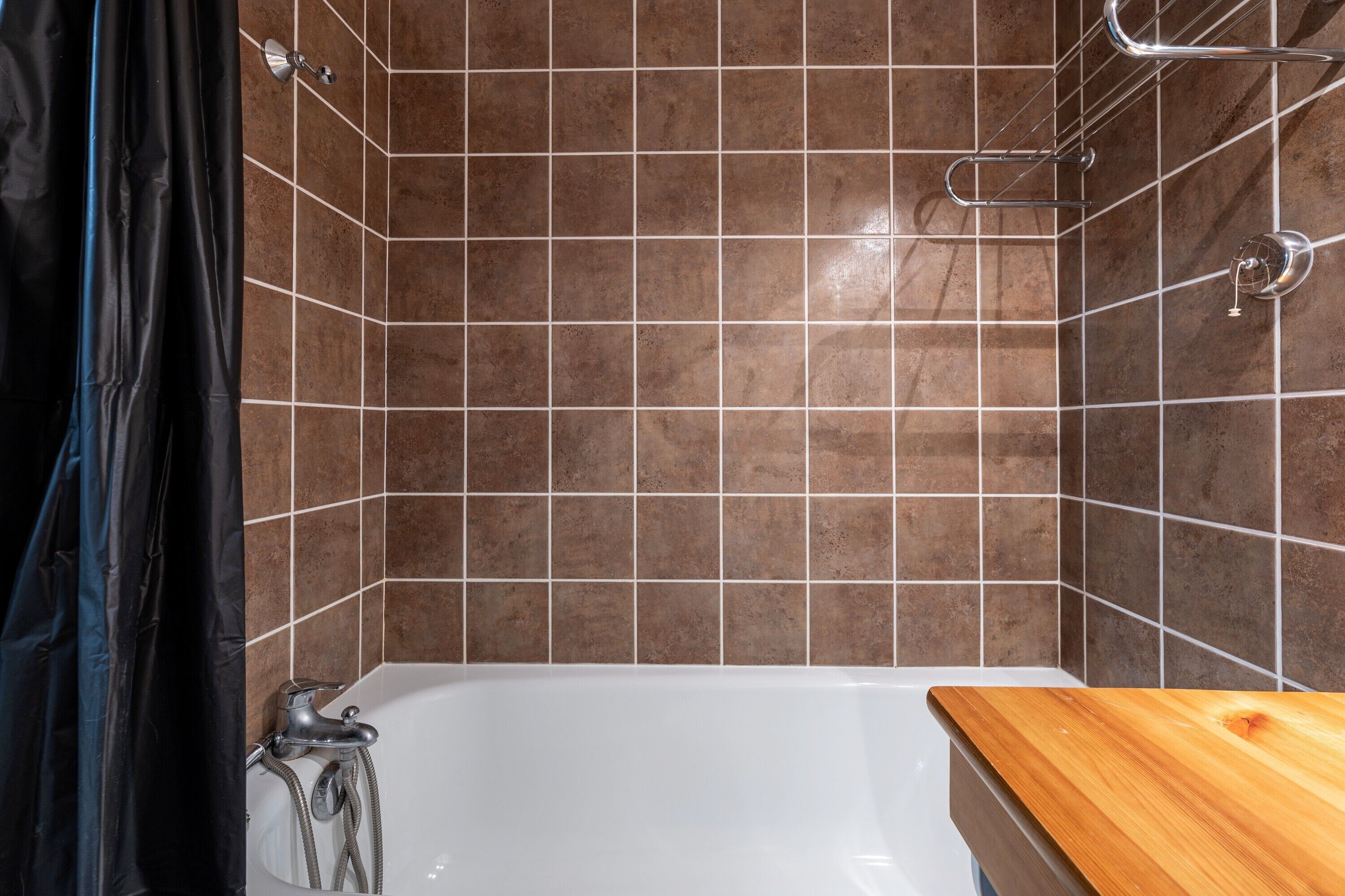 A bathroom with a bathtub, tiled walls, and a wooden countertop.