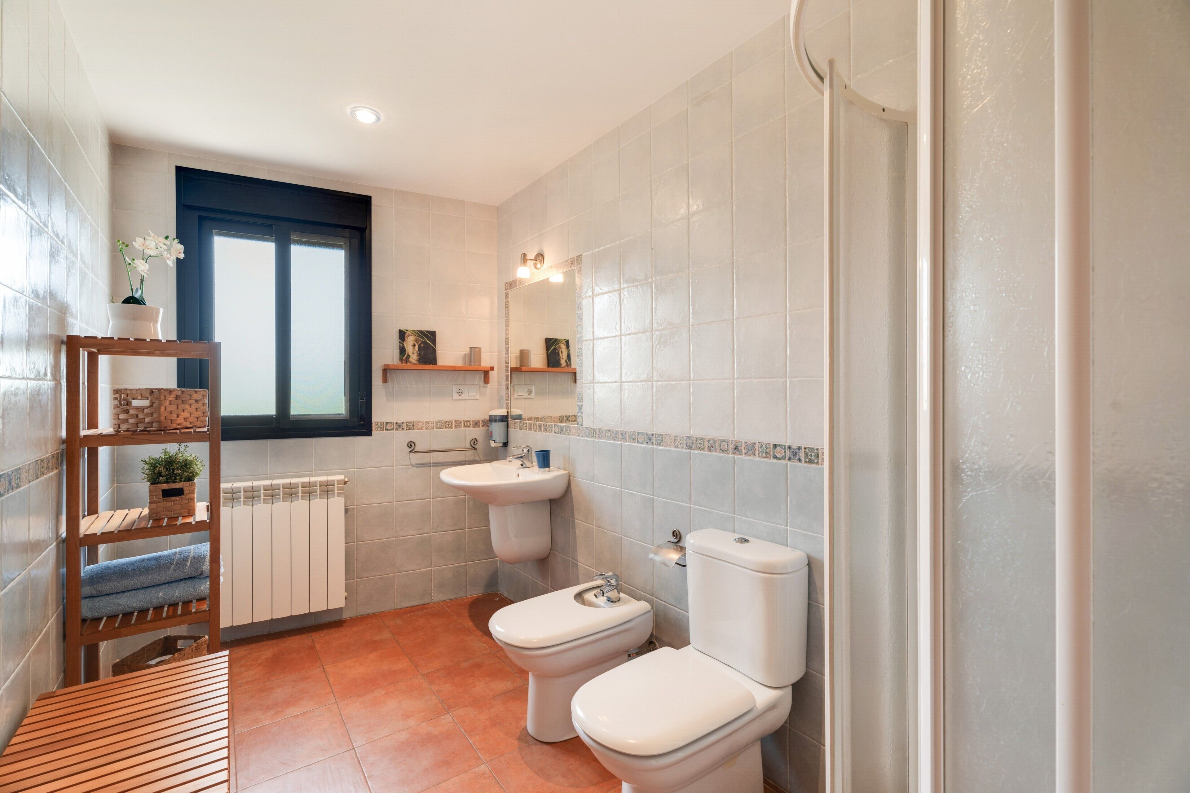 Une salle de bain avec deux toilettes, un lavabo, une fenêtre et une étagère avec des serviettes.