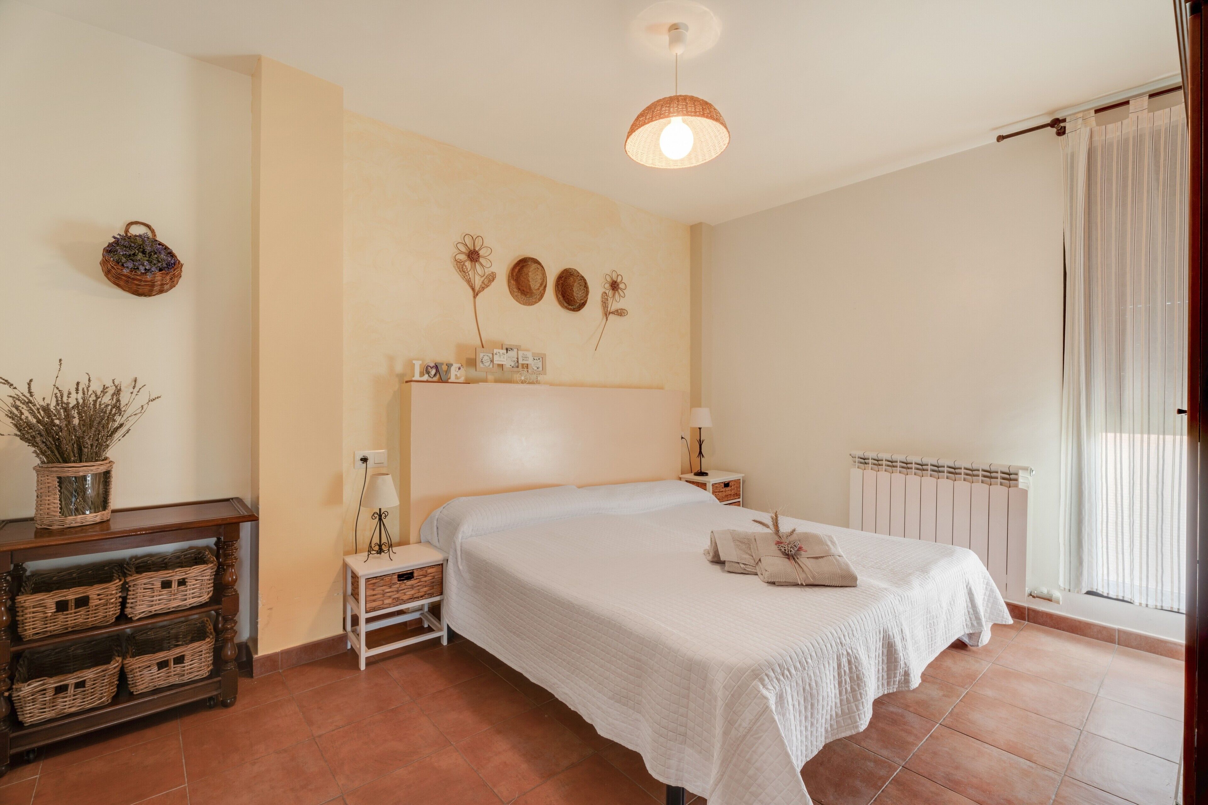 Une chambre à coucher avec un lit, des tables de chevet, une lampe, un radiateur et une fenêtre avec des rideaux.