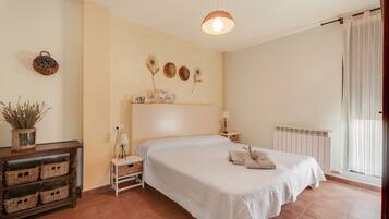 Une chambre à coucher avec un lit, des tables de chevet, une lampe, un radiateur et une fenêtre avec des rideaux.