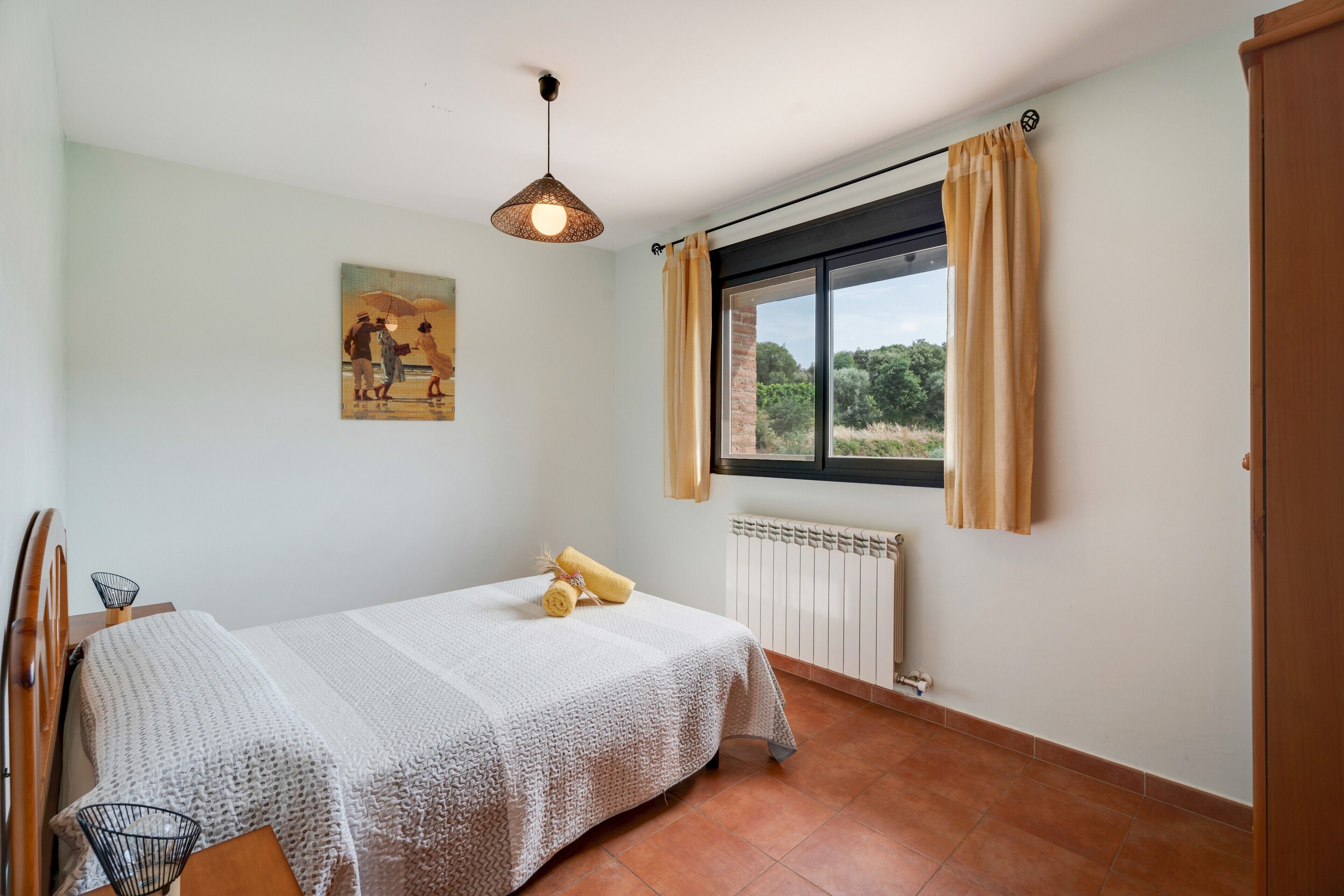 Een slaapkamer met een bed, een raam met gordijnen, een radiator en een schilderij aan de muur.