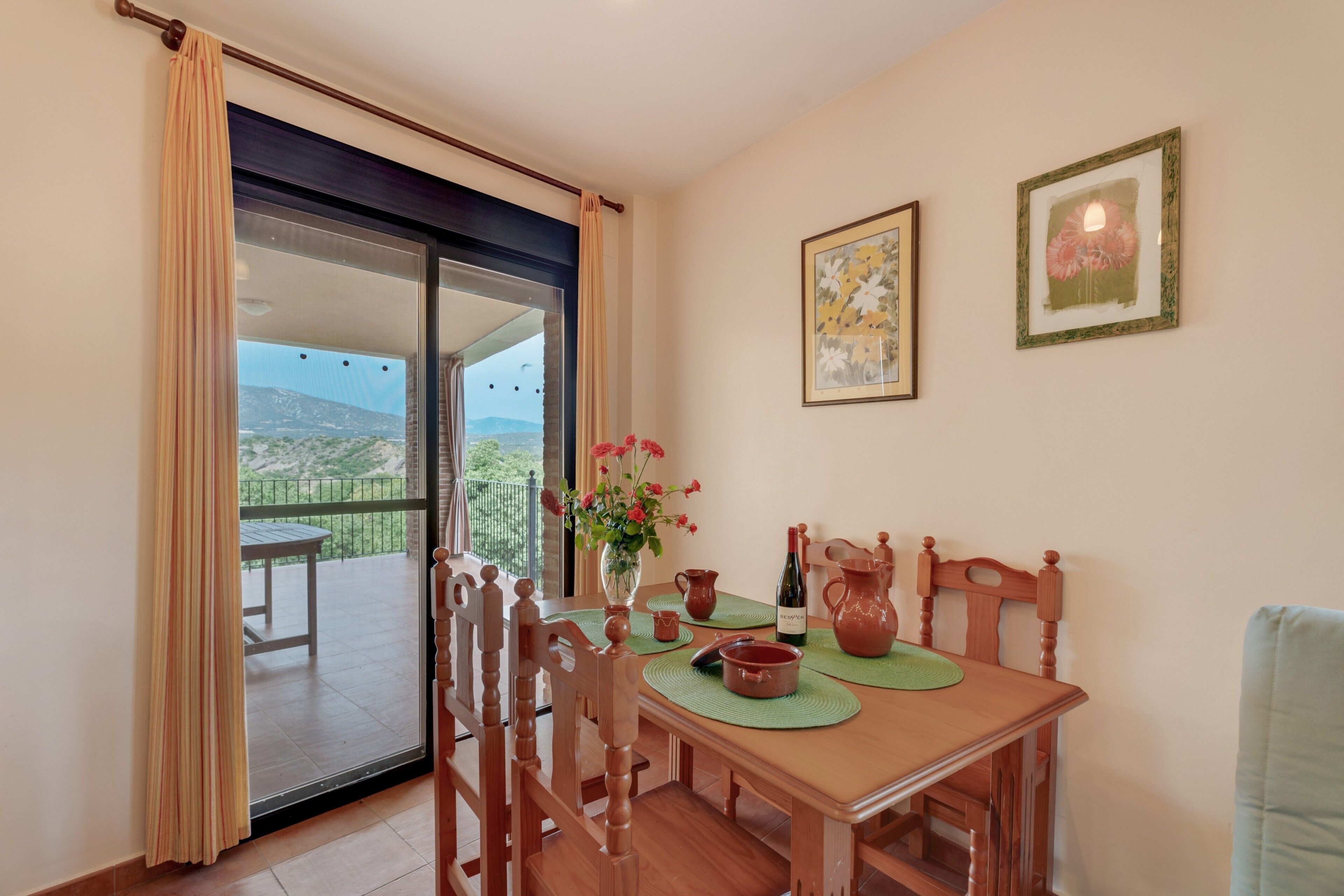 Un coin repas comprenant une table, des chaises, un vase de fleurs et une vue sur un balcon extérieur, accessible par une porte vitrée.