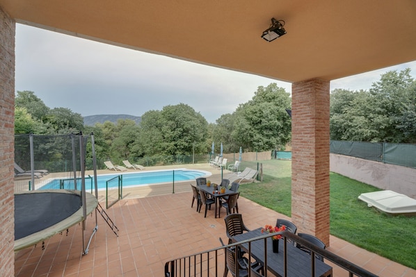 Ein überdachter Patio-Bereich mit Pool, Gartenmöbeln und Blick auf die umliegende Landschaft.