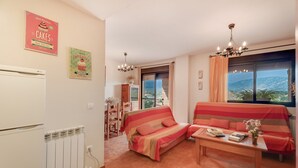 A living room with a sofa, a table with books, a radiator, and a window with a view. - Holiday Home 'Sueños De Guara Casa Rural' with Mountain Views, Private Pool and Wi-Fi (Casbas de Huesca)