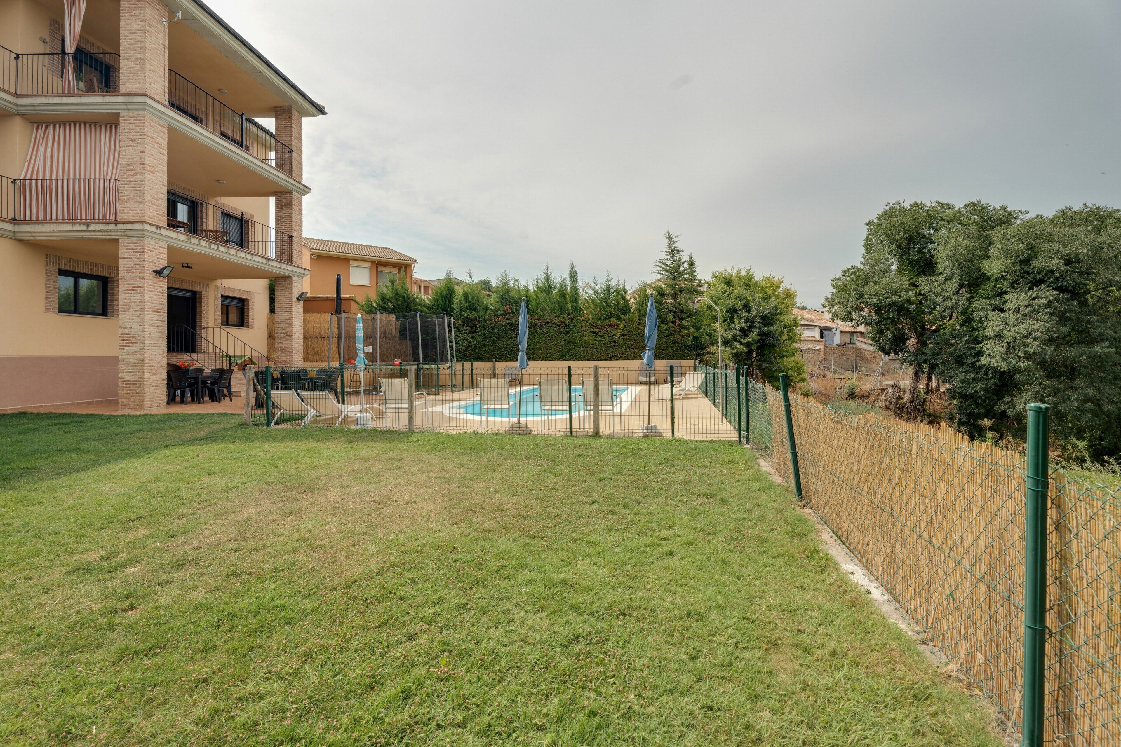Un edificio residencial con piscina, patio cercado y balcón con mobiliario exterior.