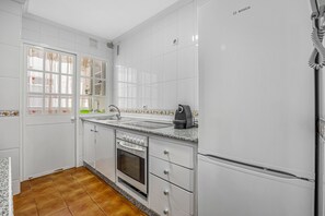 Une cuisine avec des armoires blanches, un four encastré, un évier et un réfrigérateur Bosch.