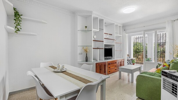 A modern living room with a dining area, white walls, and a green sofa.