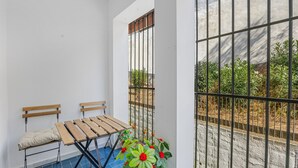 A balcony with a table and chairs, a potted plant, and a view through a barred window.