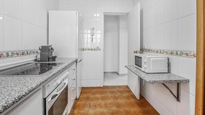 A compact kitchen with white tiles, a stove, microwave, and a small countertop.