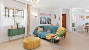 A modern living room with a green sofa, a yellow ottoman, and a cityscape painting.