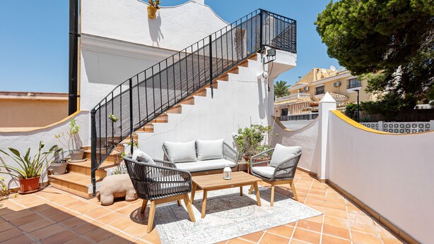 A rooftop patio with a staircase, outdoor furniture, and potted plants.