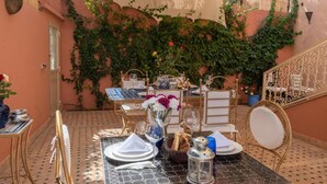 An outdoor dining area with a table set for two, surrounded by ivy-covered walls and a tiled floor. - Hôtel Riad Airport Marrakech (Marrakech)