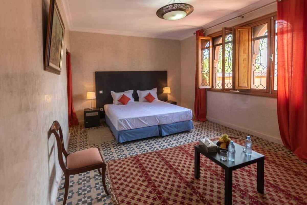 Una habitación de hotel con una cama, una silla, una mesa con objetos y una ventana con cortinas.