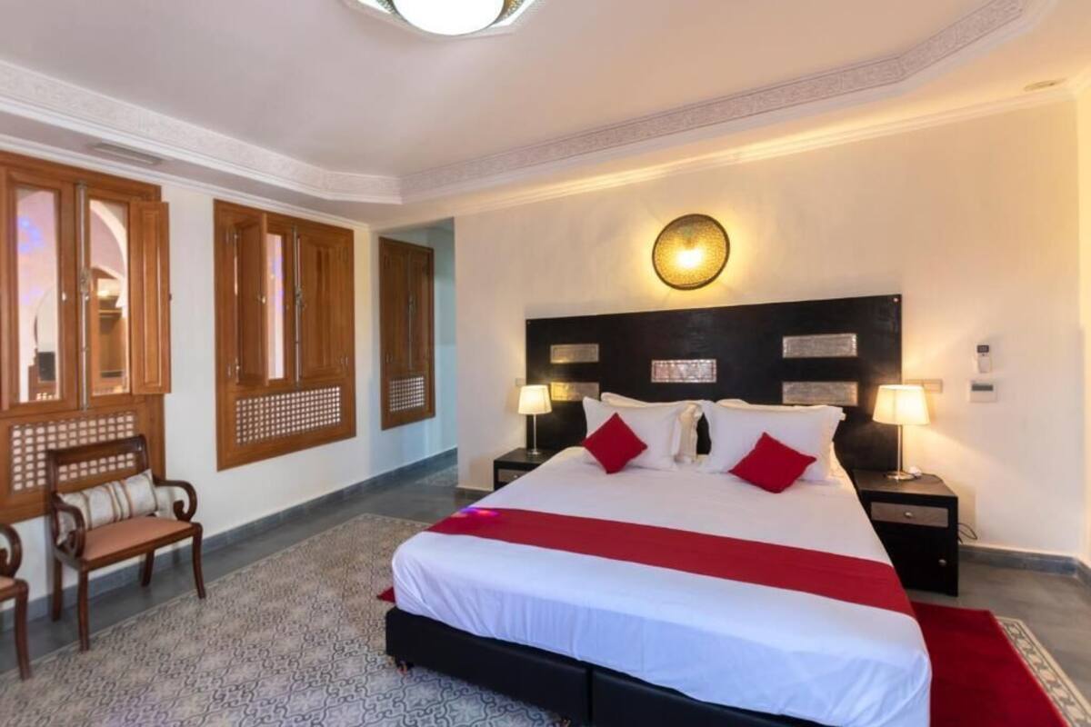 Habitación de hotel con una cama grande, dos mesitas de noche con lámparas, un banco de madera y un adorno en la pared.