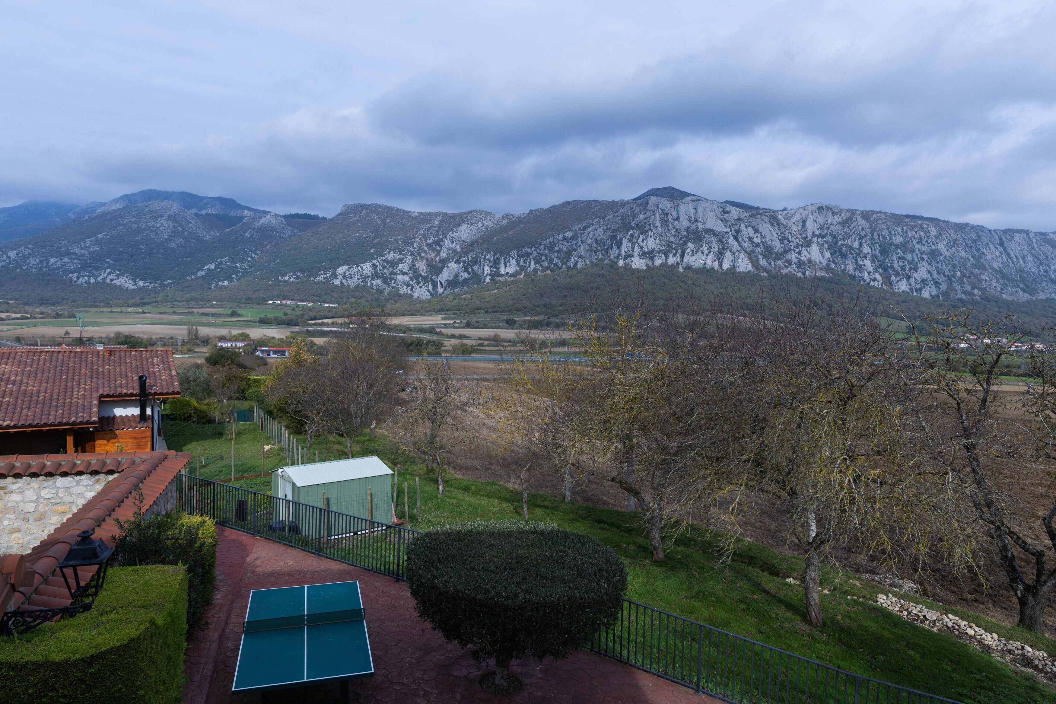Un paisaje montañoso con una casa que tiene techo de tejas rojas y una cancha de tenis verde.