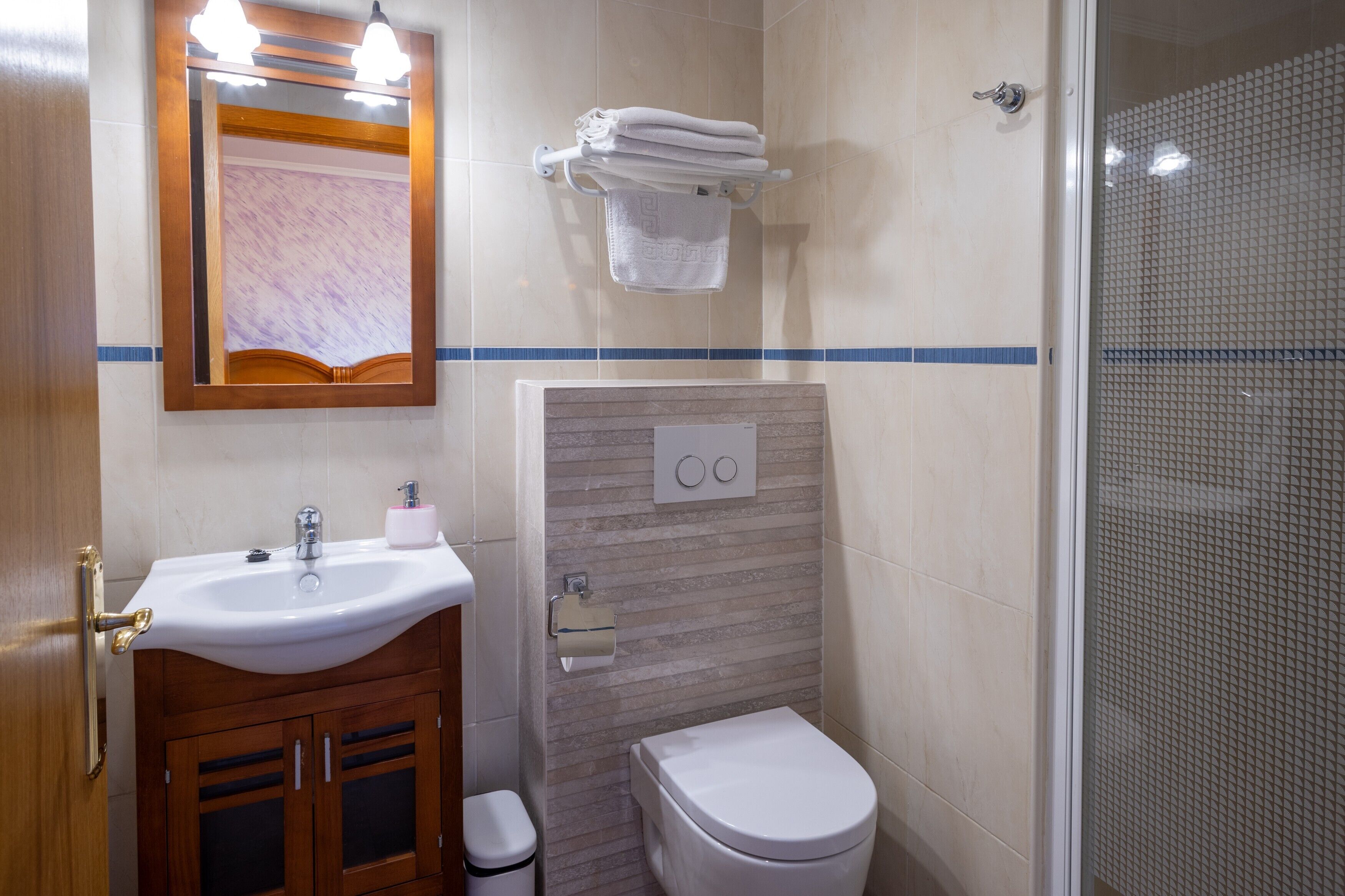A bathroom with a sink, mirror, towel rack, toilet, and shower.