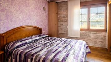 A bedroom with a wooden bed, a stone wall, and a window with a view of mountains.