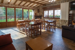 A spacious living area with a stone fireplace, wooden furniture, and large windows offering views of a garden.