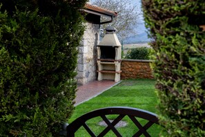 A stone barbecue grill with a chimney, surrounded by a well-maintained lawn and a stone wall.