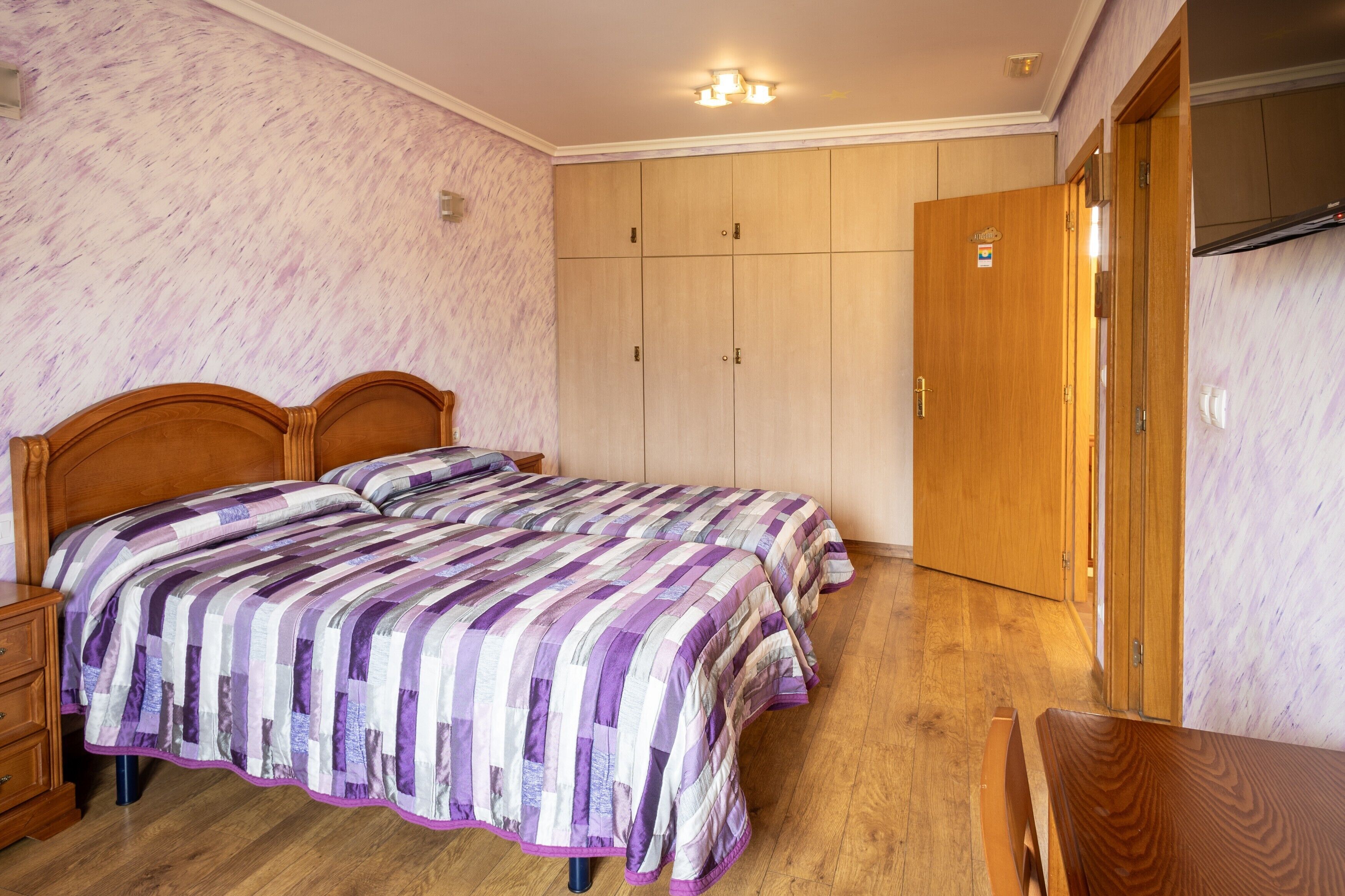 A bedroom with two wooden beds, a wooden wardrobe, and a wooden table.