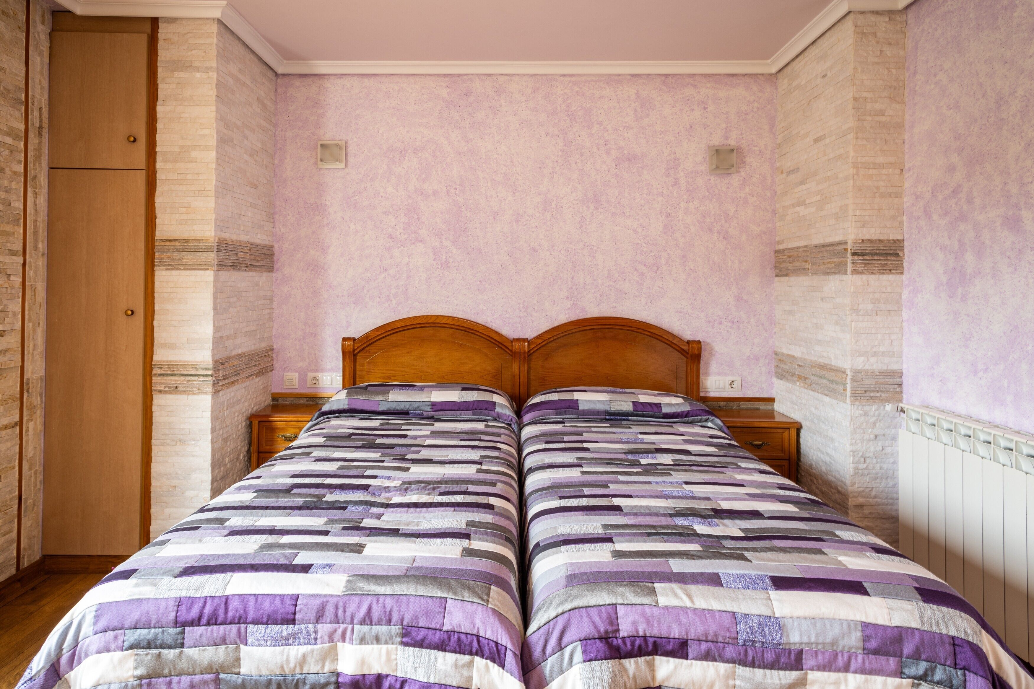Un lit double avec une couvre-lit à motifs, une tête de lit en bois, des tables de chevet, une armoire et un radiateur.