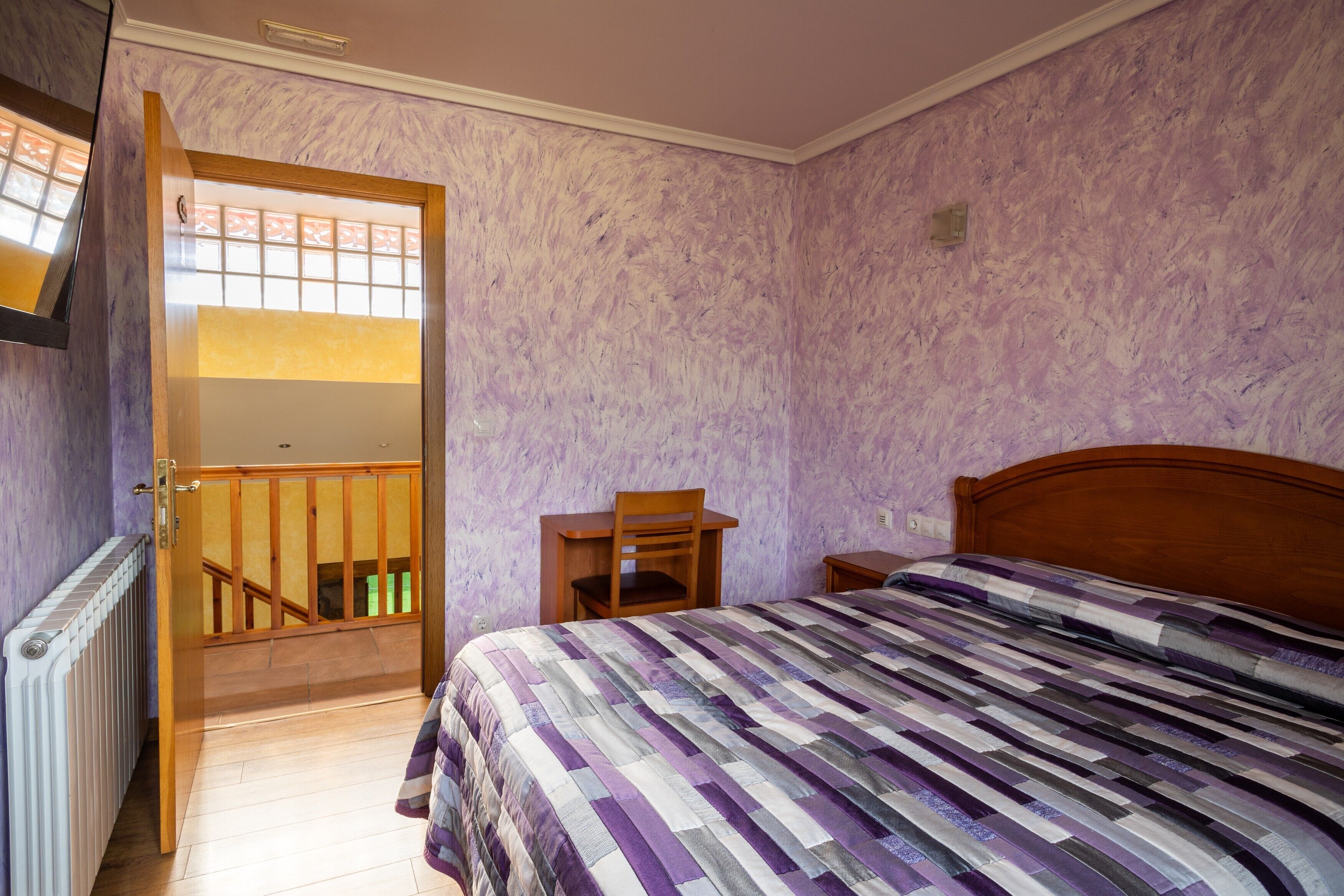 Una camera da letto con un letto, una sedia in legno, un tavolino e una scala che conduce a un piano superiore.