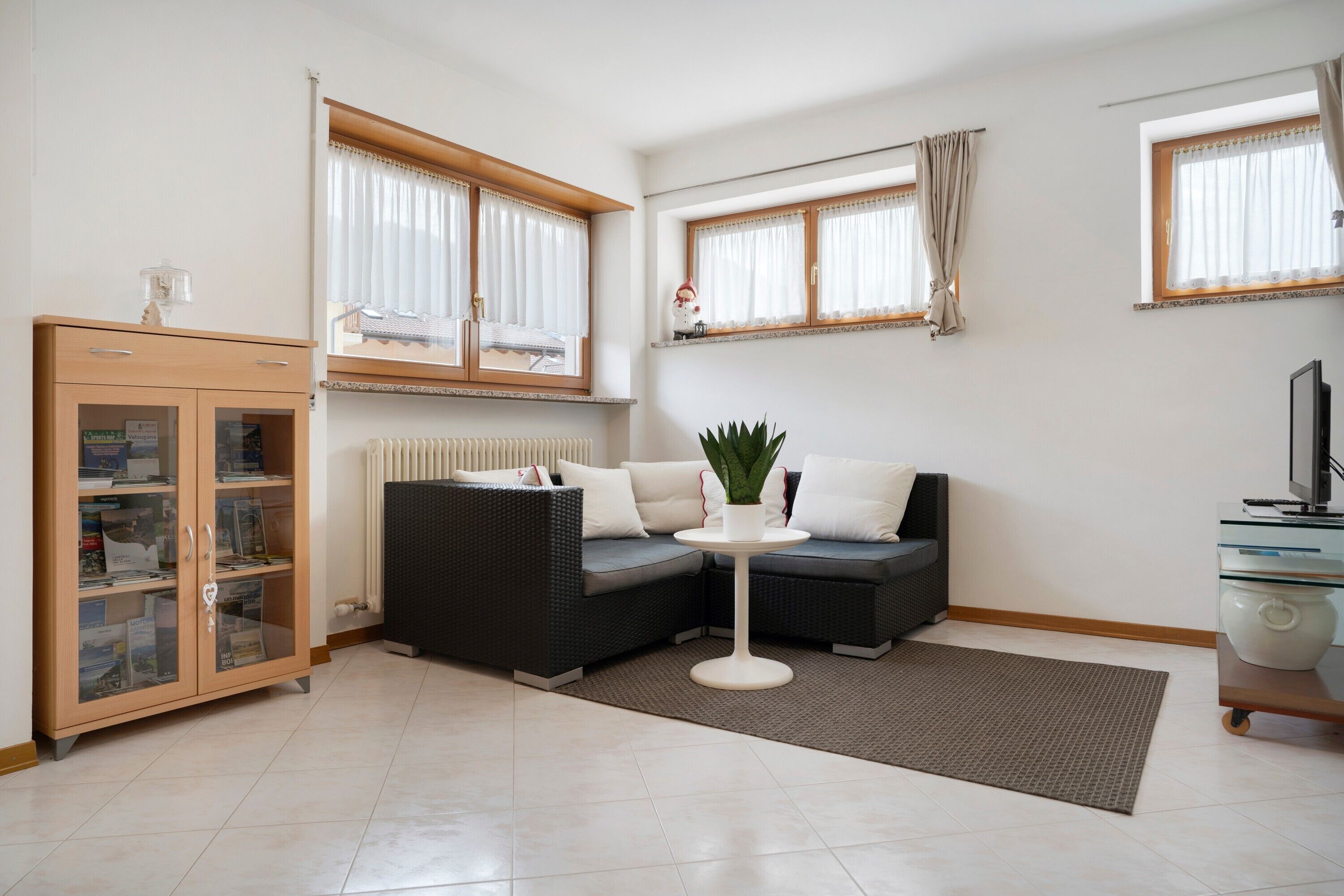 A modern living room with a sectional sofa, a small round table, a cabinet with glass doors, and a radiator.