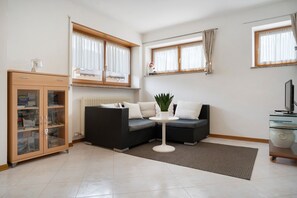 A modern living room with a sectional sofa, a small round table, a cabinet with glass doors, and a radiator.