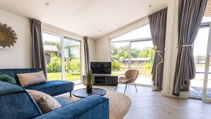 Un soggiorno moderno con un divano blu, una televisione e vista su un giardino attraverso ampie finestre.