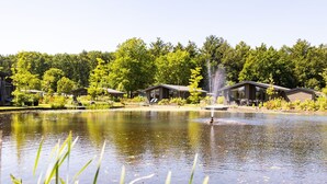 Un paesaggio tranquillo sul lago con una fontana, immerso nel verde rigoglioso e circondato da moderne cabine.