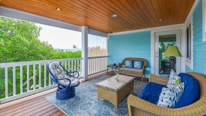 A covered porch with wicker furniture, a view of greenery, and a door leading inside. - Lux Canal Front 4 bedroom - Home w/ Dock, Near Looe Key – Fishing, Diving & Sunsets! (Ramrod Key)