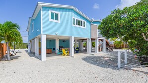 A two-story house with a covered porch, a small outdoor seating area, and a gravel driveway. - Lux Canal Front 4 bedroom - Home w/ Dock, Near Looe Key – Fishing, Diving & Sunsets! (Ramrod Key)