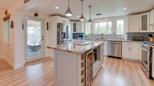 A modern kitchen with white cabinets, stainless steel appliances, and a large island with a marble countertop. - Lux Canal Front 4 bedroom - Home w/ Dock, Near Looe Key – Fishing, Diving & Sunsets! (Ramrod Key)