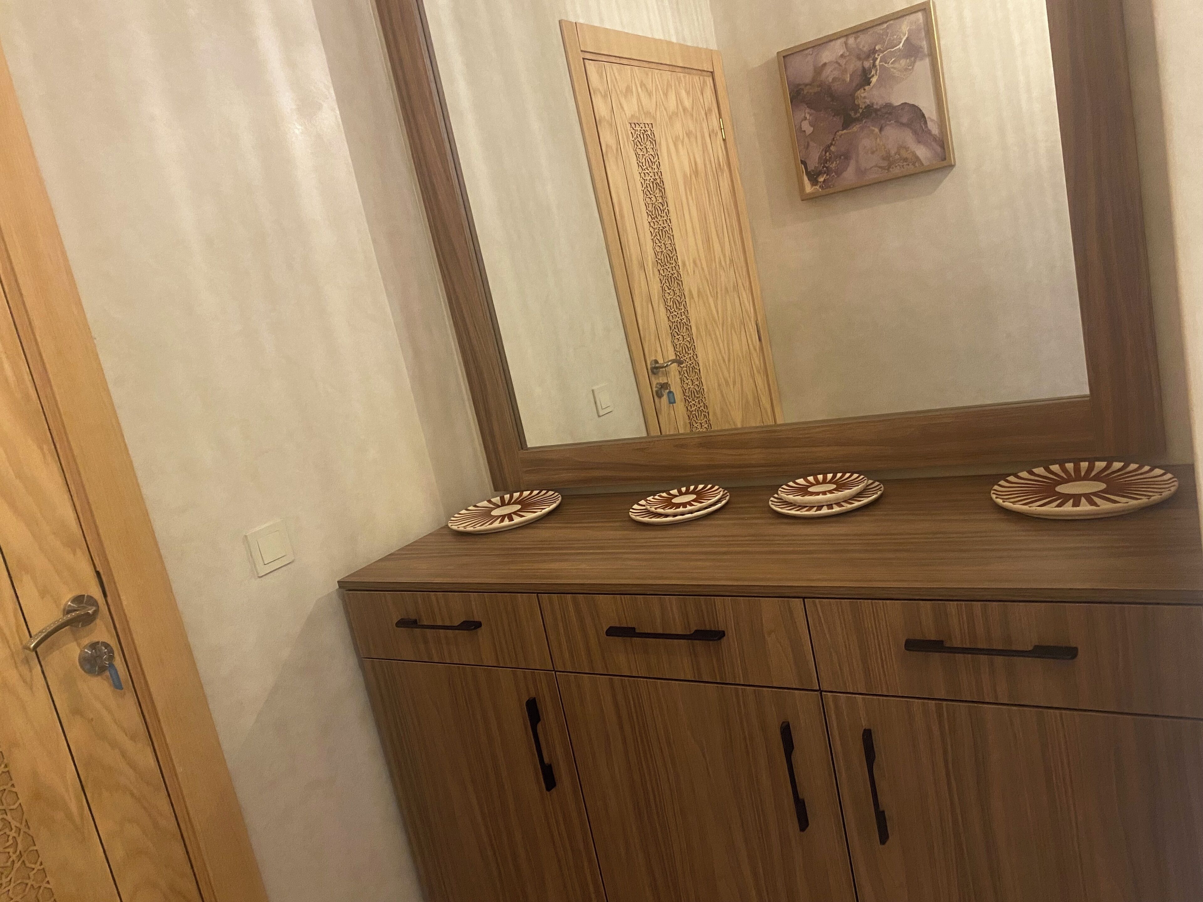 Un meuble en bois orné de quatre assiettes décoratives sur le dessus et d’un miroir qui reflète une porte aux sculptures complexes.