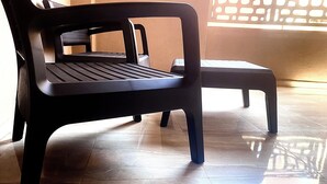Une chaise en plastique noir, dotée d’un siège et d’un dossier à lattes, placée sur un sol carrelé.