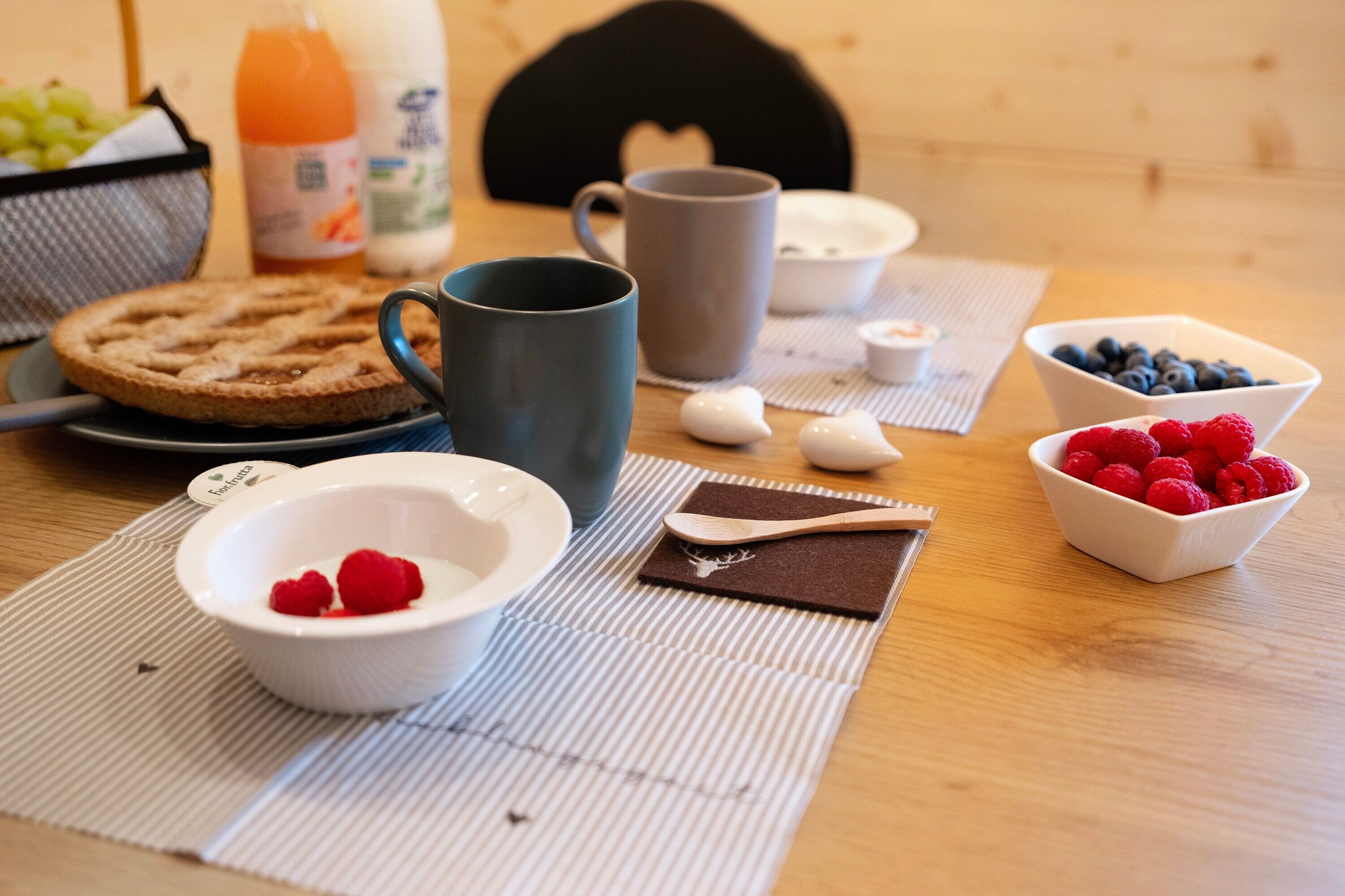 Une table en bois dressée pour le petit-déjeuner, avec un gaufre, une tasse, un bol de fruits rouges et une bouteille de jus d’orange.