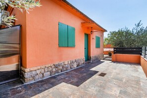 Un bâtiment avec des fondations en pierre, des murs orange, des volets verts et un patio carrelé.