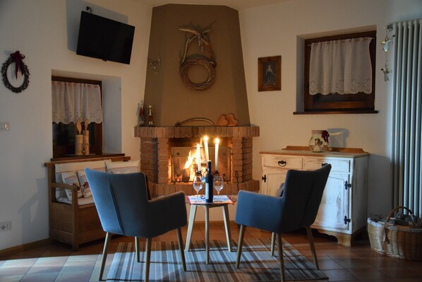 Un salon chaleureux avec une cheminée, deux fauteuils, une petite table et un téléviseur fixé au mur.