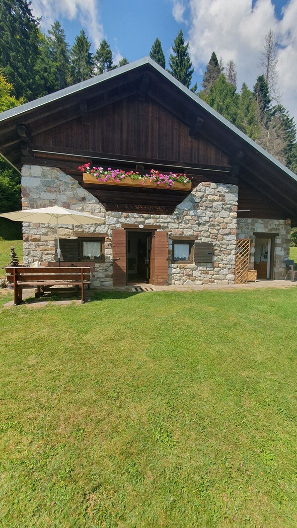 Ein Steinhaus mit Holzdach, einer Bank und einem Blumenkasten.