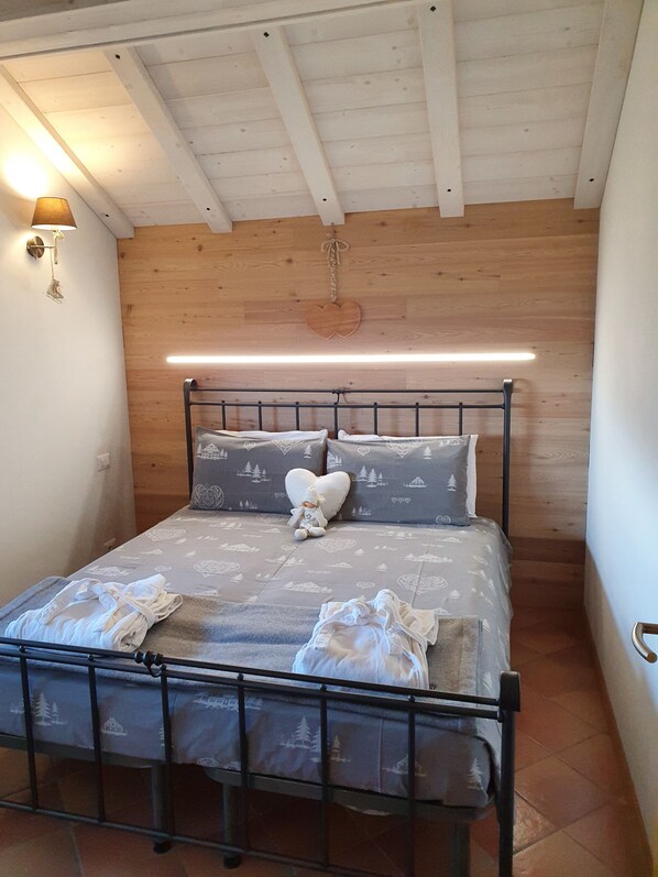Ein Schlafzimmer mit Bett, Kissen, einer herzförmigen Dekoration, einer Wandleuchte und einer Holzbalkendecke.