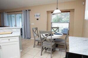 A kitchen with a dining table, chairs, a hanging light fixture, a window with blinds, and a wall-mounted sign.