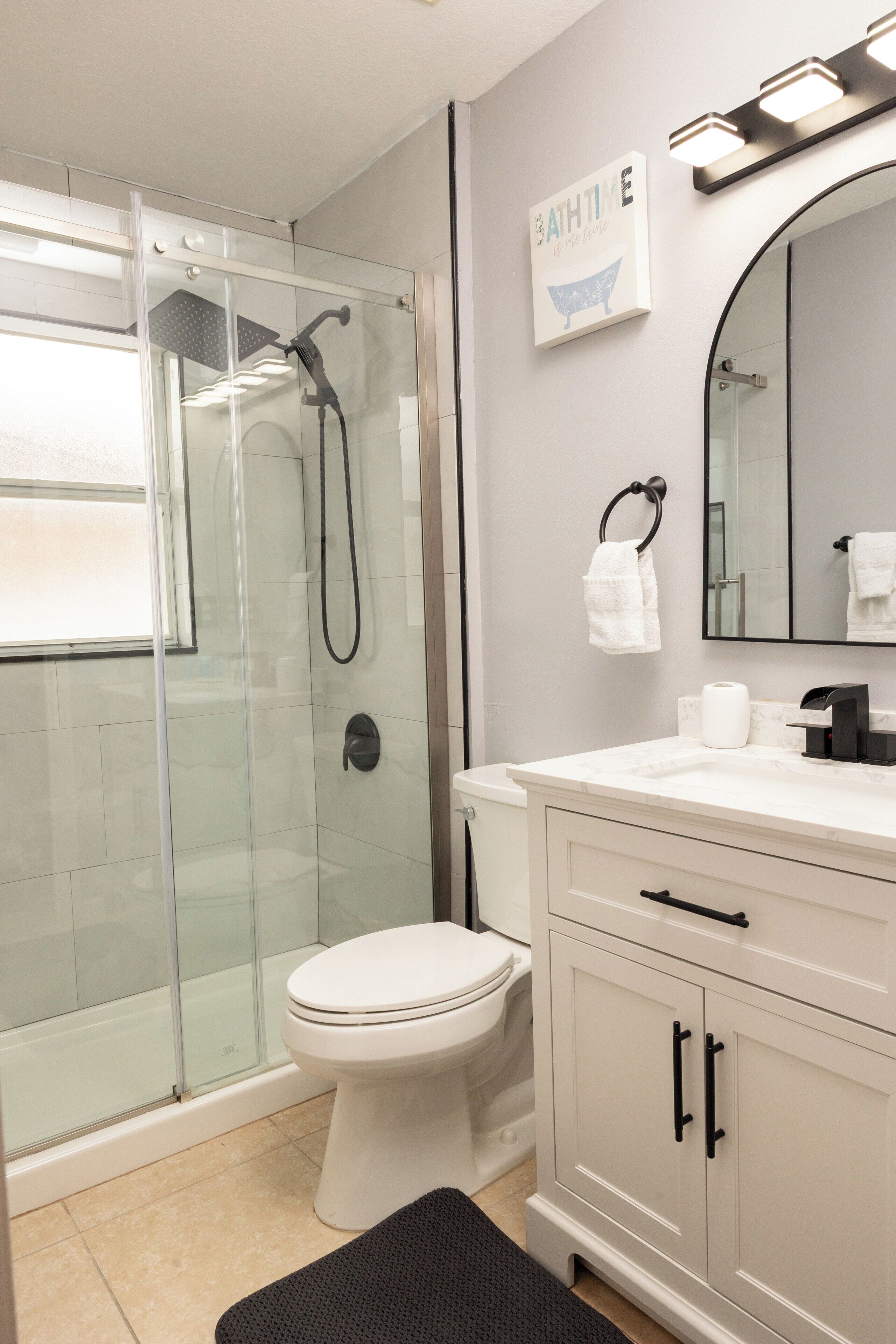 Un baño con ducha de vidrio, inodoro, lavabo con espejo y un perchero para toallas.