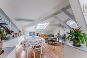 An attic room with a dining table, chairs, a sofa, and a small table with a plant.