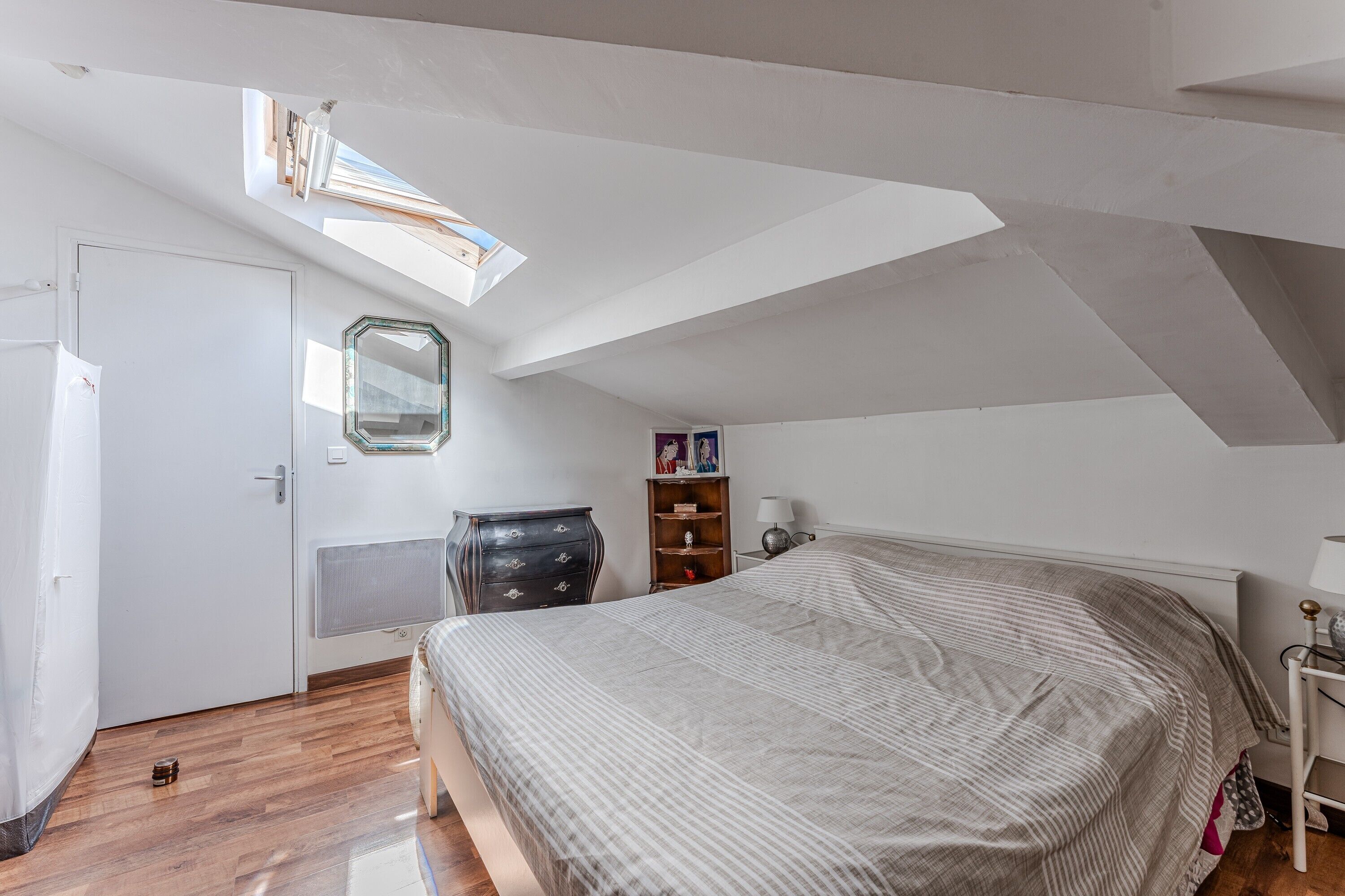 Een slaapkamer met dakraam, een bed, een dressoir en een nachtkastje.