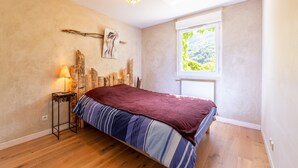 A bedroom with a bed, a window, a lamp, and a wall-mounted picture.