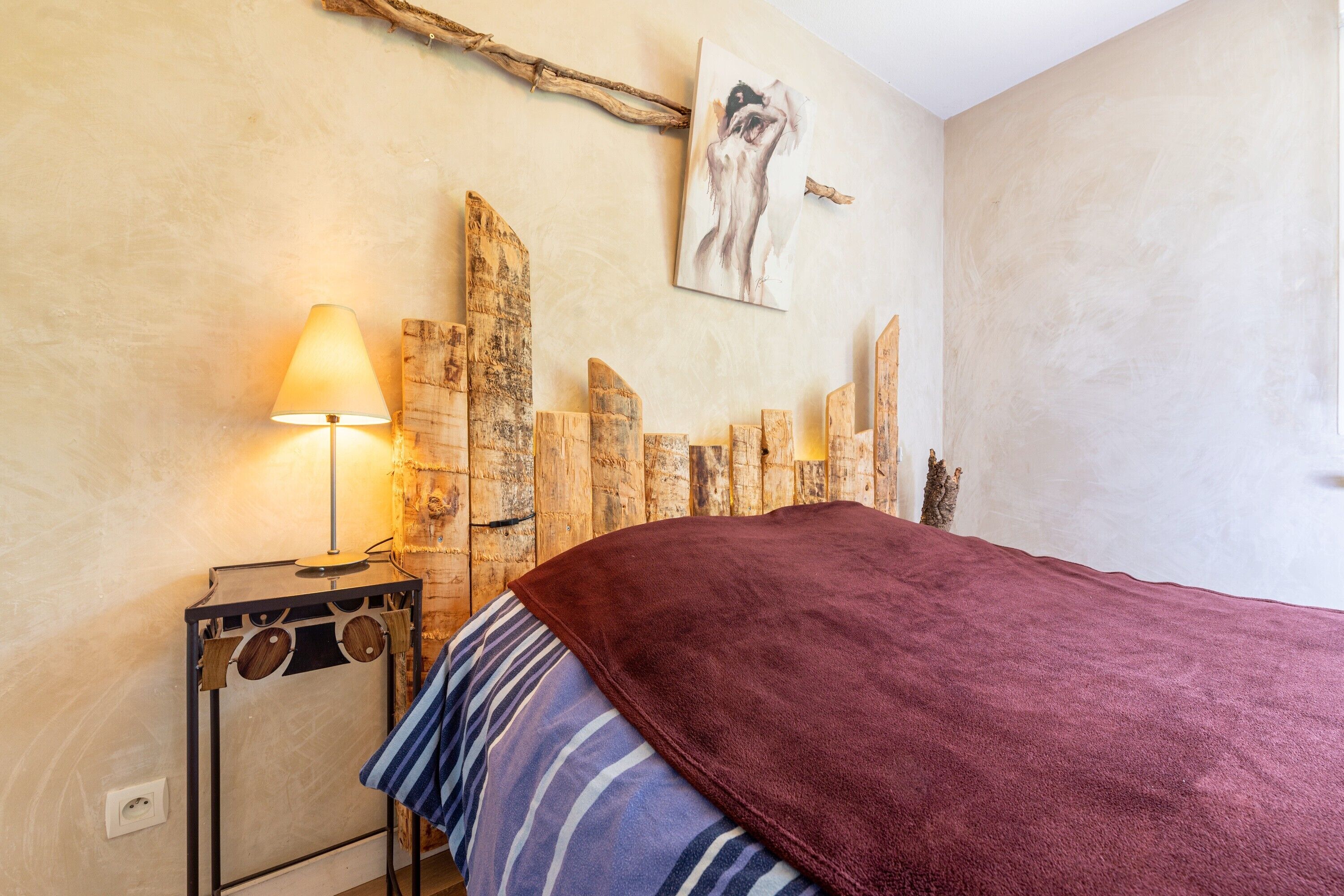 Um quarto com uma cama, uma luminária, um quadro na parede e um adorno de madeira na parede.