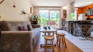 A modern living room with a sofa, wooden stools, a dining table, and a kitchen area with a bar.